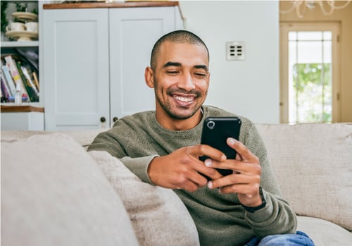 Mann sitzt auf hellem Sofa und hält mit beiden Händen ein Handy