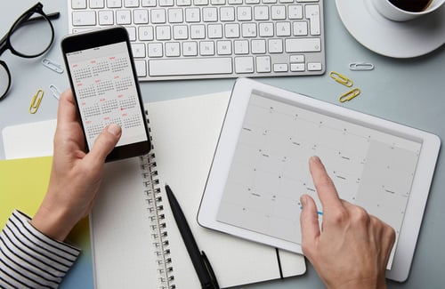 Person von oben, die ein Smartphone und einen Terminkalender in der Hand hält