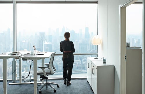 Business-Frau in schwarzer Kleidung von hinten im Büro schaut aus dem Fenster