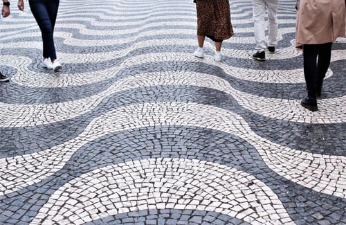 Fünf Personen gehen über ein Mosaikpflaster mit einem großen schwarz-weißen Wellenmuster auf dem Fußgängerüberweg in Lissabon, Portugal