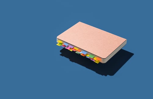 Notizbuch mit bunten Lesezeichen in der Luft schwebend auf blauem Hintergrund.