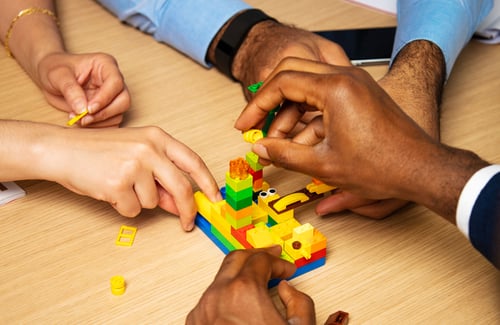 Nahaufnahme von 3 Händen von Menschen verschiedener Hautfarben, die Legosteine zusammenbauen