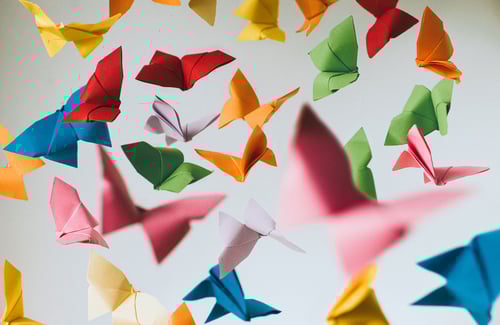 Bunte Origami Schmetterlinge flattern vor grauem Hintergrund